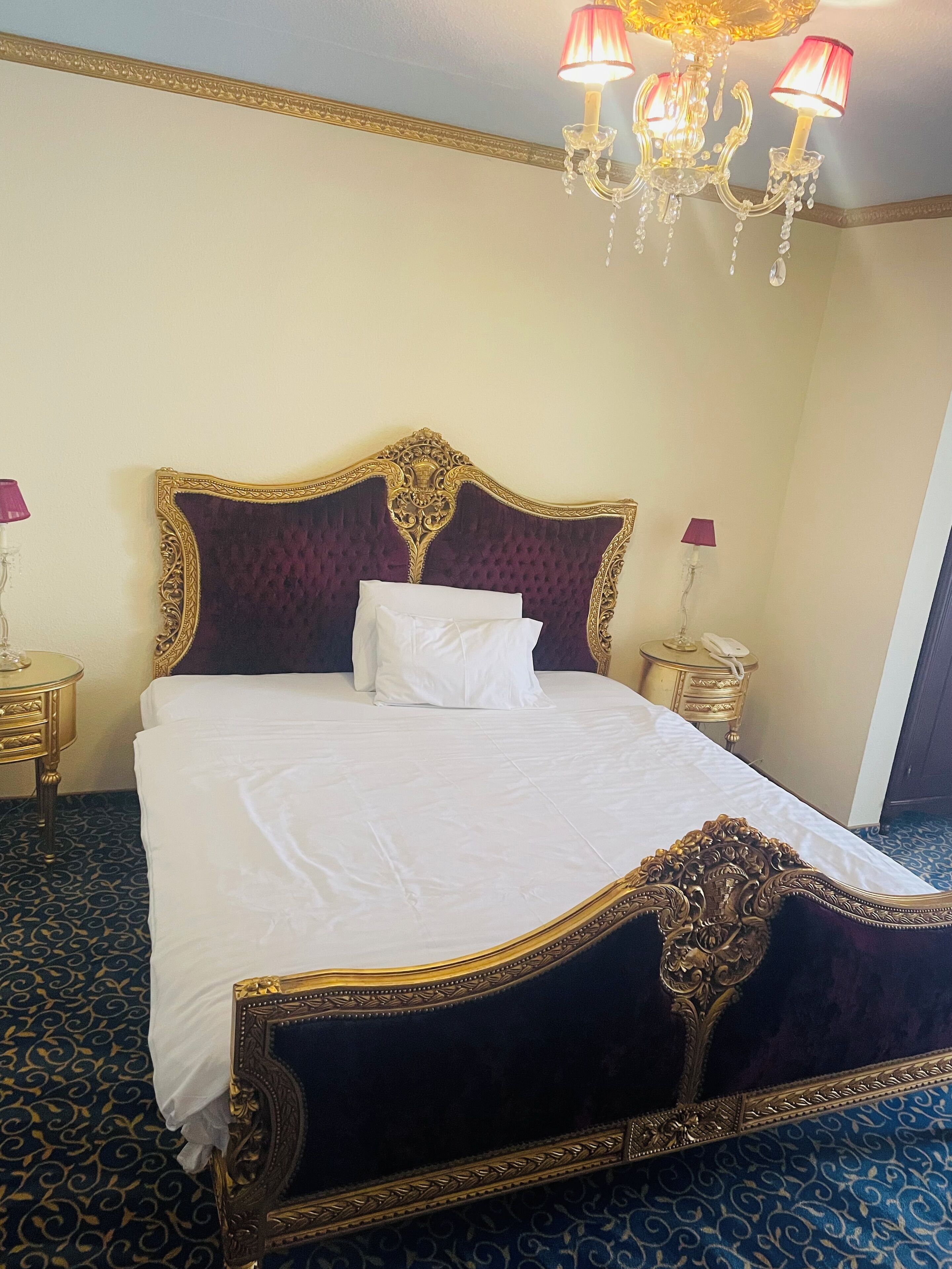 Una habitación de hotel con una cama grande, un cabecero decorado y una araña.