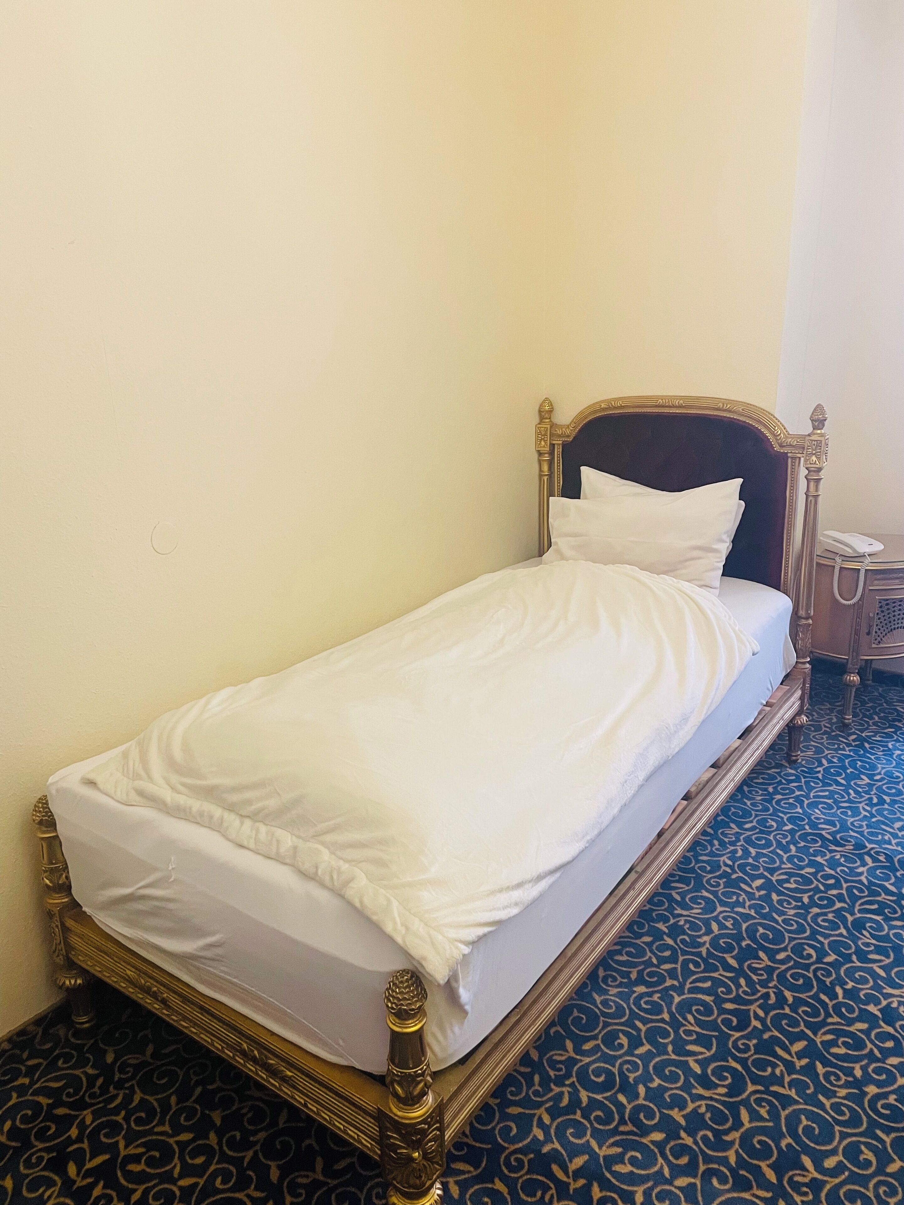 A single bed with a wooden frame and white bedding in a room with patterned carpet.