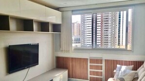 Ein modernes Wohnzimmer mit Wand-Fernseher, einer eingebauten Regaleinrichtung, einem Fenster mit Jalousien und einer gepolsterten Sitzecke.