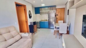 Ein kompakter Wohnbereich mit Sofa, Esstisch, Fernseher und Küchenzeile, ausgestattet mit blauen Schränken und einem Kühlschrank.