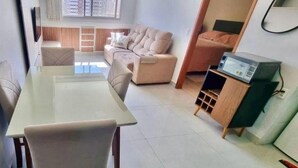 Ein modernes Wohnzimmer mit einem Esstisch aus Glas, beigen Sofas und einer Holzkommode mit einem Fernseher.