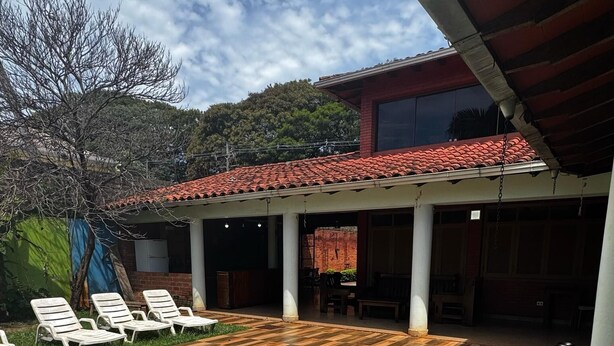 Un espacio al aire libre techado con piscina, sillones de descanso y vistas a una colina.