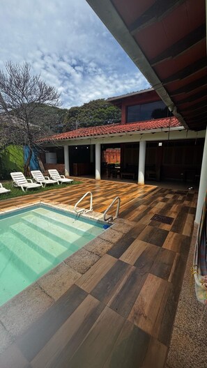 Un espacio al aire libre techado con piscina, sillones de descanso y vistas a una colina.