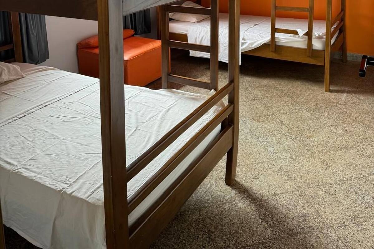 Een slaapkamer met stapelbed, plafondventilator, raam met gordijnen en een oranje muur.
