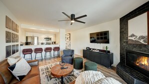 A modern living room with a fireplace, a ceiling fan, and a kitchen in the background. - Gorgeous Remodeled 3-Bedroom home in charming downtown Frisco with Private Sauna (Frisco)