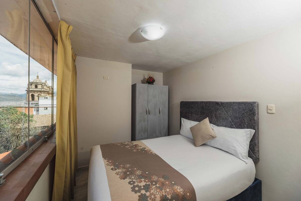A hotel room with a bed, a wardrobe, and a window with curtains.