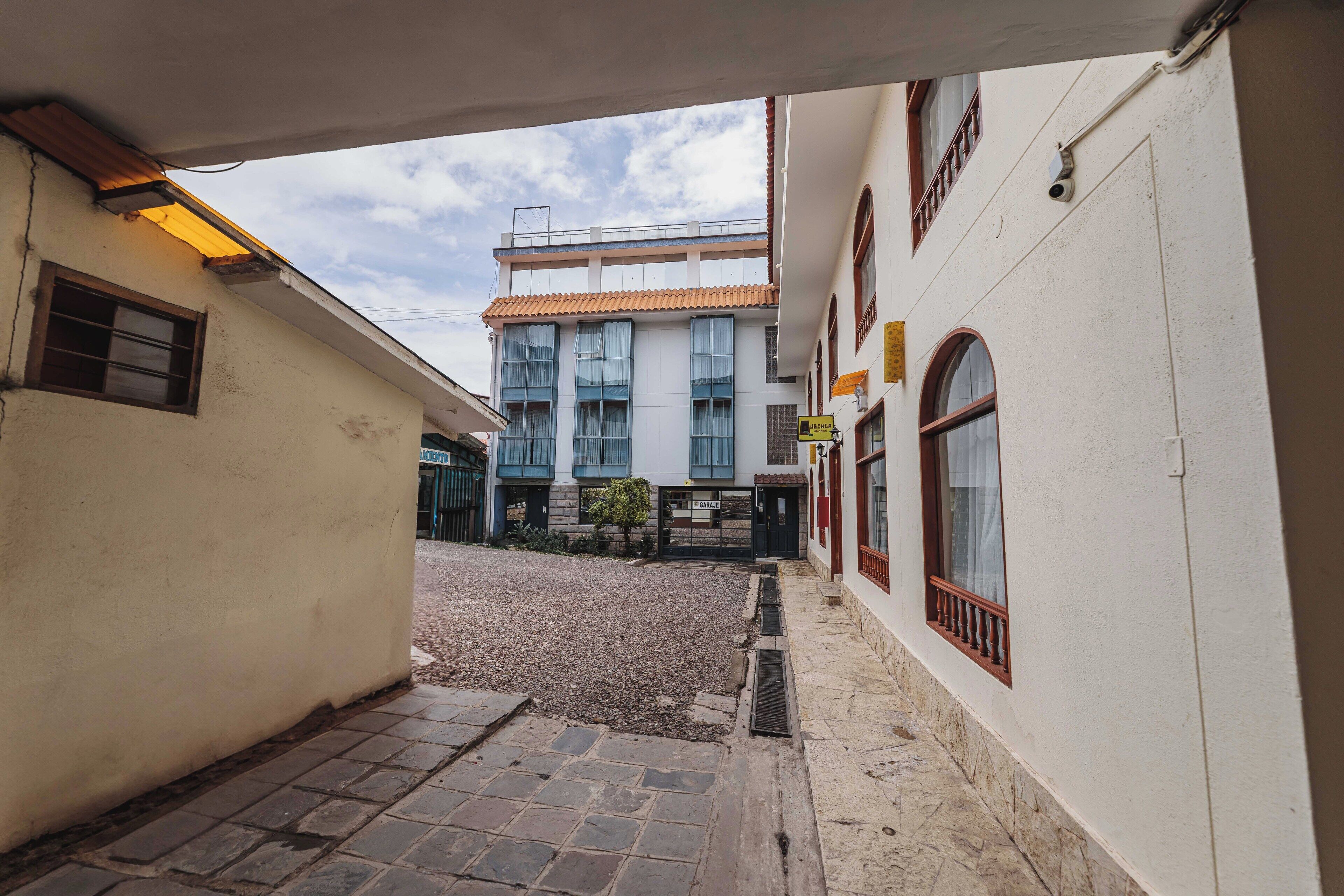 A narrow alleyway with cobblestone pavement leading to a building with a tiled roof and multiple windows.