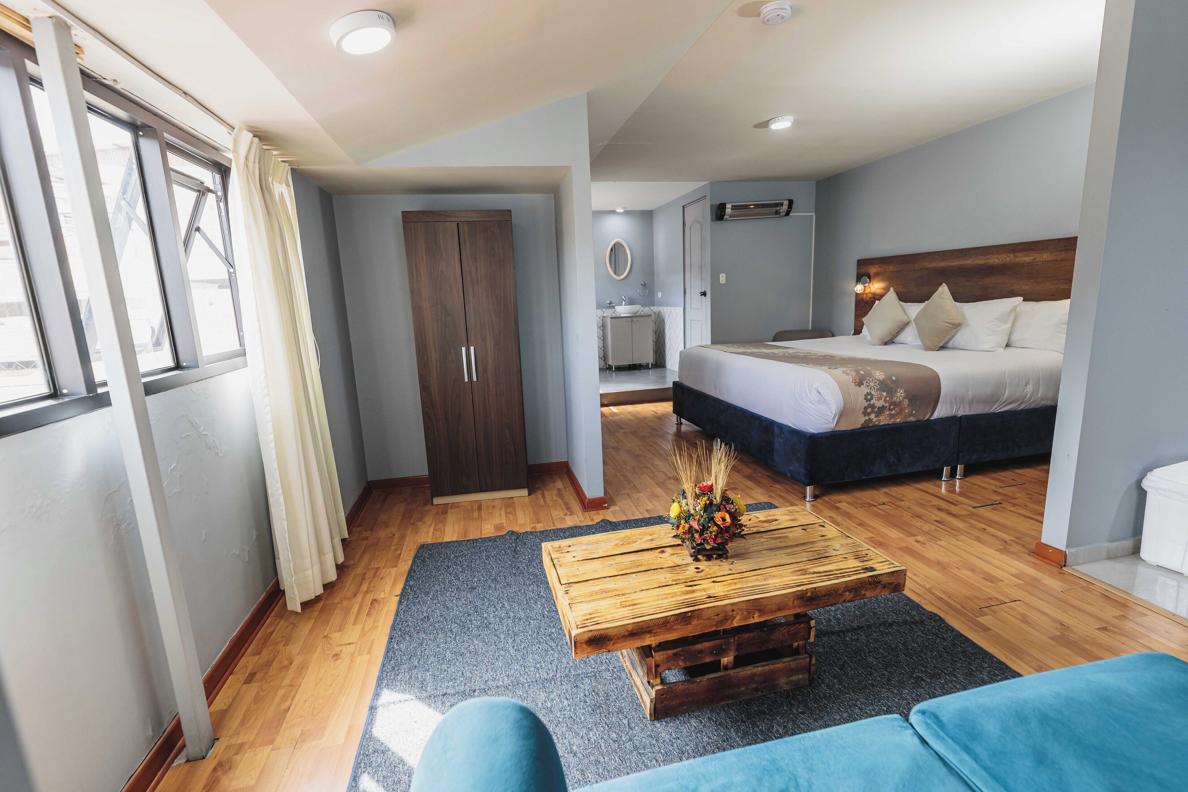A bedroom with a bed, a wooden coffee table with a flower arrangement, a wardrobe, and a bathroom visible in the background.
