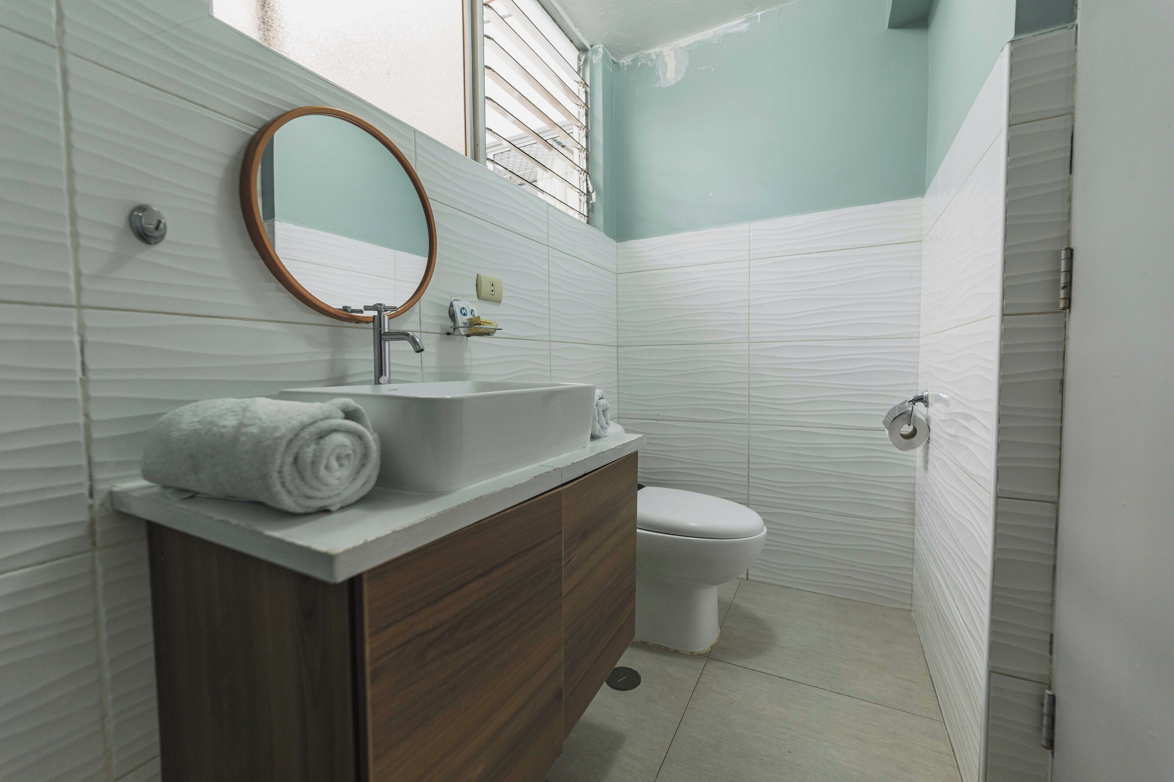 Un baño con tocador de madera, lavabo blanco, espejo y retrete.