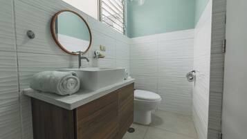 Un baño con tocador de madera, lavabo blanco, espejo y retrete.