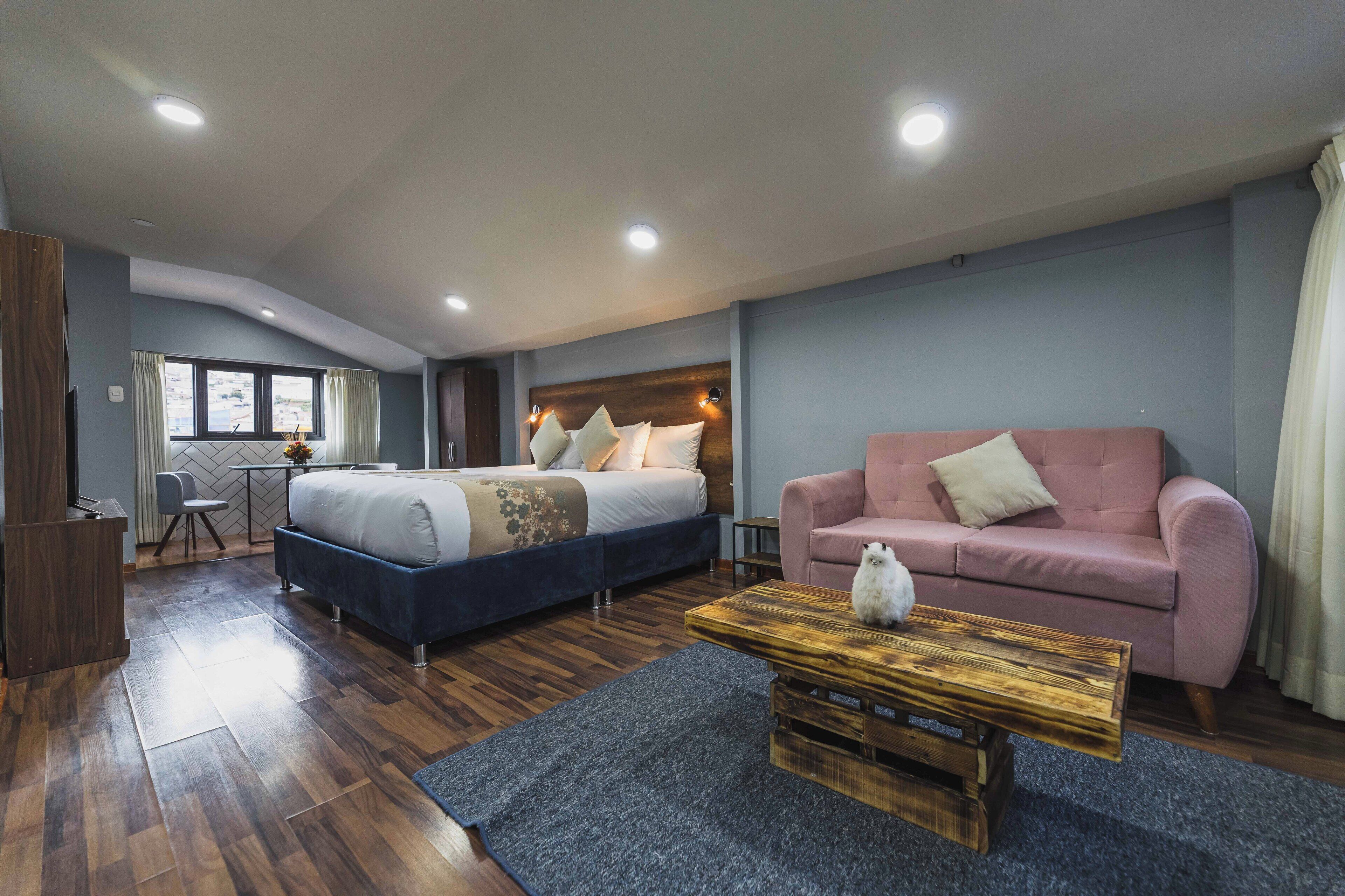 A modern hotel room with a bed, a sofa, a wooden coffee table, and a desk.