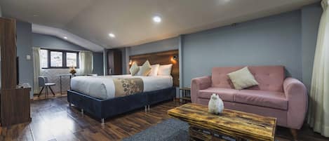 A modern hotel room with a bed, a sofa, a wooden coffee table, and a desk.