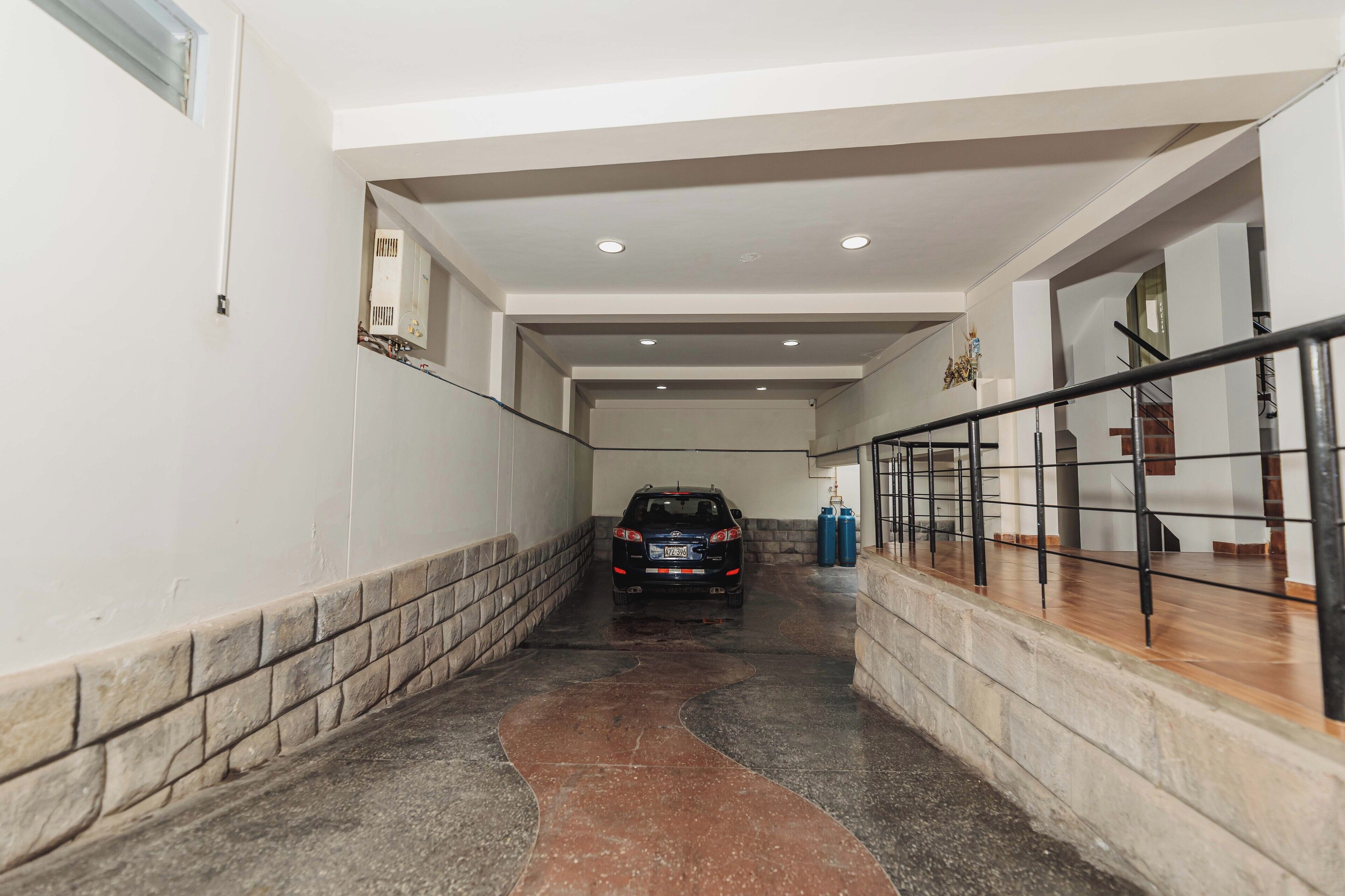 Un automóvil estacionado en un área de estacionamiento techada, con piso mojado, una escalera y una barandilla.