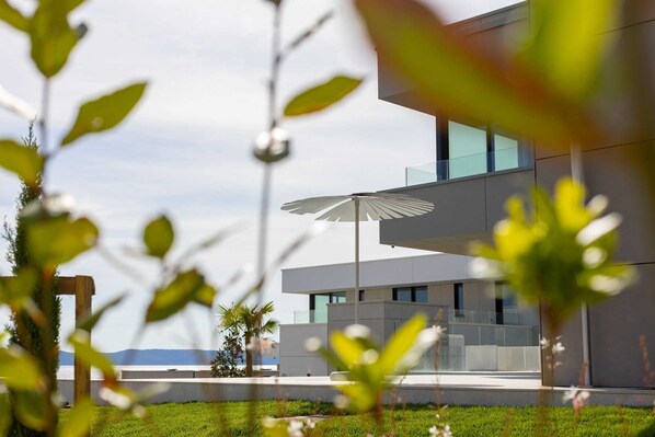 A modern building with a glass facade, a white umbrella, and a view of the sea.