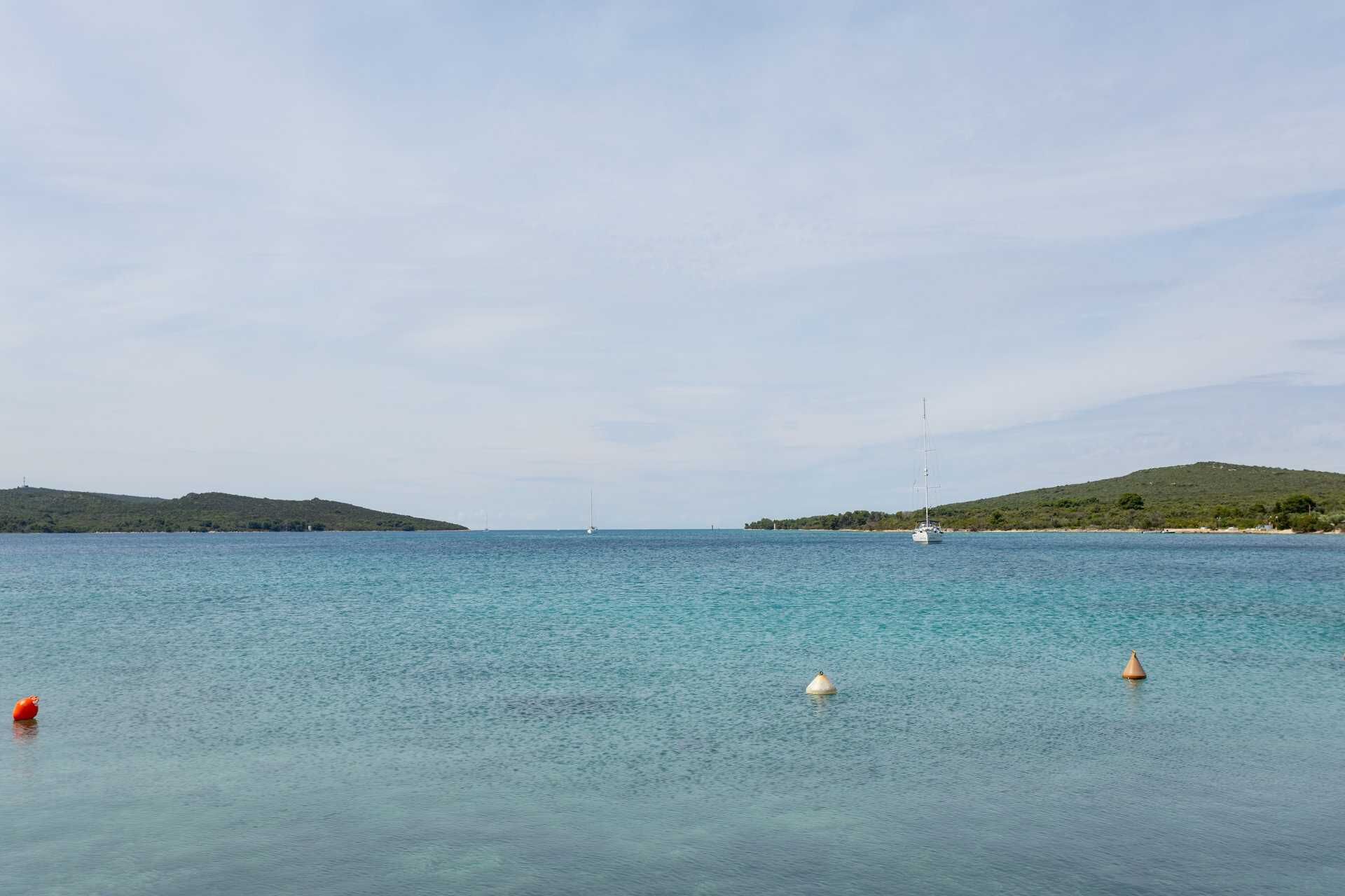 Ruhige See mit Bojen und einem entfernten Segelboot.