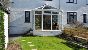 A white house with a conservatory, a garden with stepping stones, and a wooden bench. - 3 bedroom accommodation in Keswick (Keswick)
