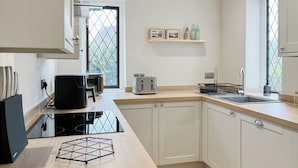 A modern kitchen with white cabinets, a black stove, a toaster, and a sink. There is a window with a view of greenery outside. - 3 bedroom accommodation in Keswick (Keswick)