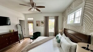 A bedroom with a bed, a dresser, a chair, a ceiling fan, a window, and a TV. - Dreamland in the Brooklyn Arts District (Wilmington)