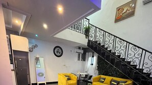 A modern living room with a black marble floor, yellow sofas, and a staircase with decorative railings. - Residence Tade (Douala)