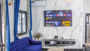 A modern living room with a blue sofa, a flat-screen TV mounted on the wall, and a marble-patterned wall. - Residence Tade (Douala)