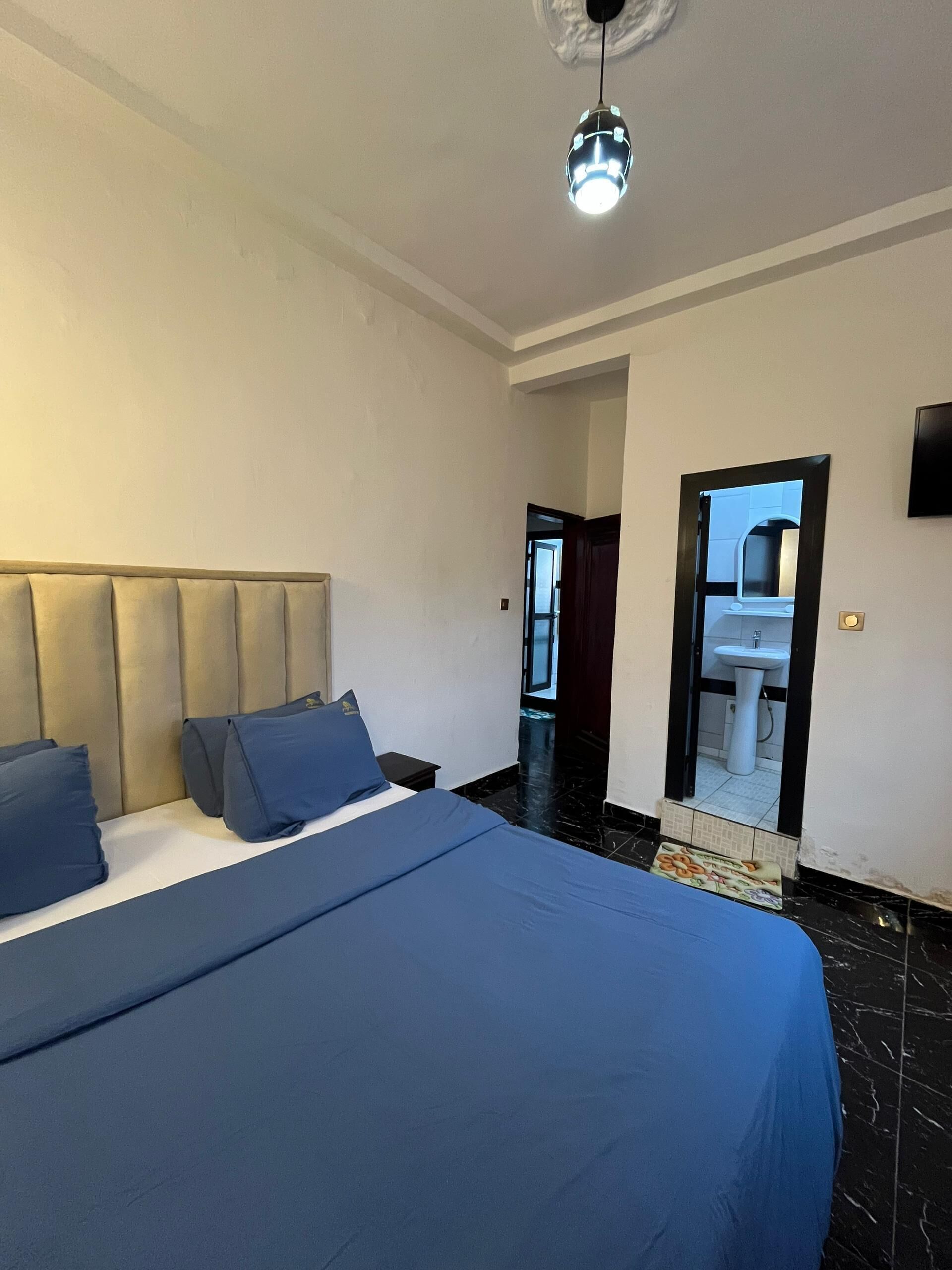 A bedroom with a large bed, a headboard, a nightstand, a mirror, and a ceiling light.