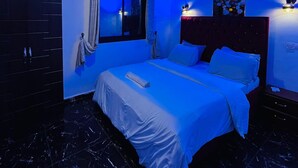A modern bedroom with a large bed, a ceiling light, an air conditioning unit, a window with curtains, and a wall-mounted artwork. - Residence Tade (Douala)