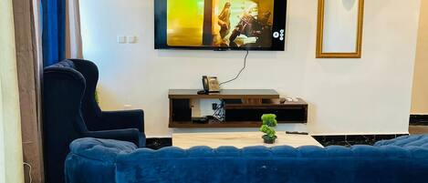 A modern living room with a blue sofa, a mounted TV, a chandelier, and a small plant on a wooden console table.