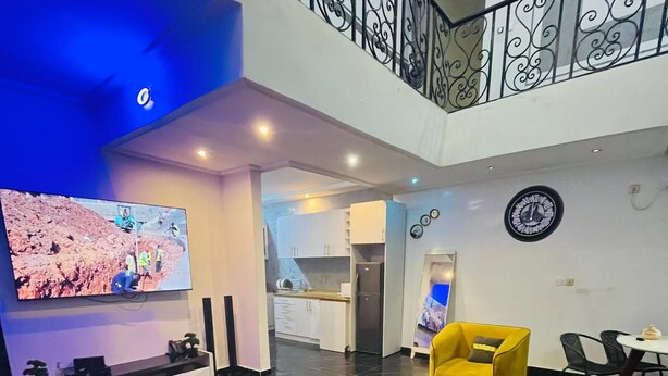 A spacious living area with yellow armchairs, a flat-screen TV, and a kitchen in the background. - Residence Tade (Douala)