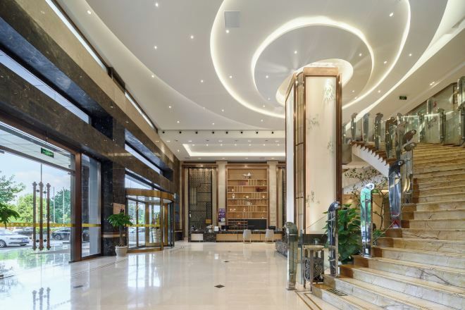 A spacious lobby with a marble staircase, a reception desk, and a large glass entrance.