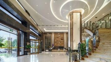 A spacious lobby with a marble staircase, a reception desk, and a large glass entrance.