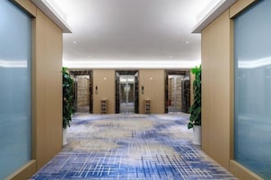 Vestíbulo de hotel con piso estampado, ascensores y puertas de vidrio.