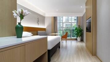 A modern hotel room with a bed, bedside table, and a large window offering a view.