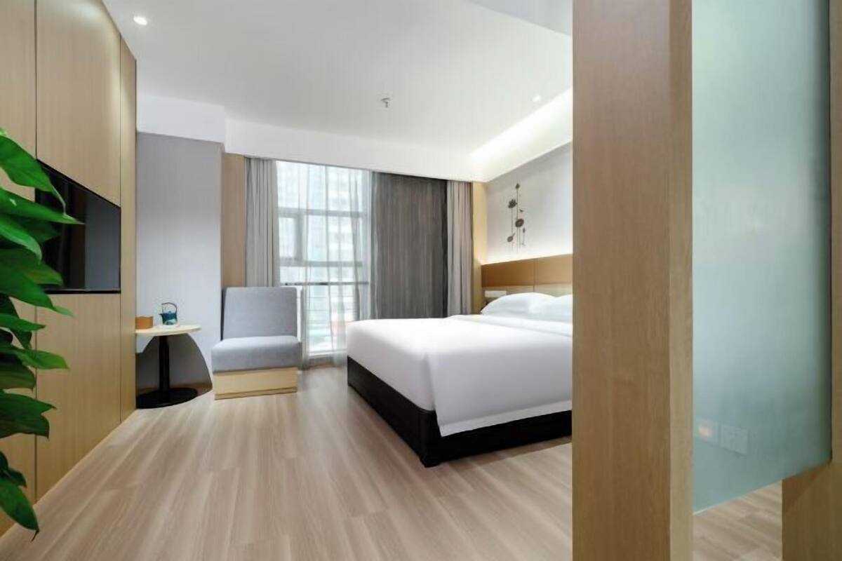 A modern hotel room with a bed, a desk, a chair, and a large window.