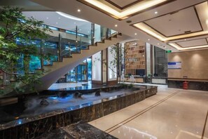 A modern hotel lobby with a marble reception desk, a hot spring, a staircase, and a glass railing overlooking the lobby. - Kaili Hotel Suining (Suining)