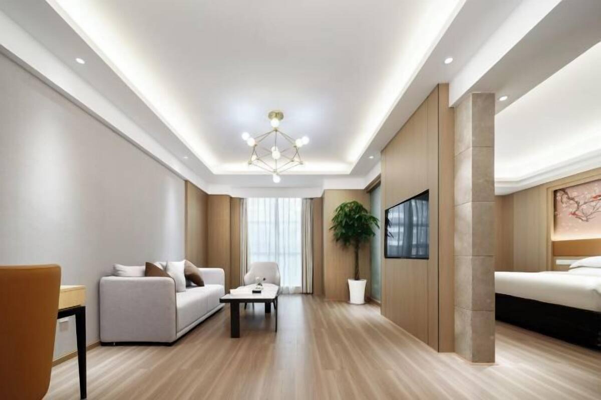 A modern hotel room with a sofa, a coffee table, a bed, a TV, and a large window.