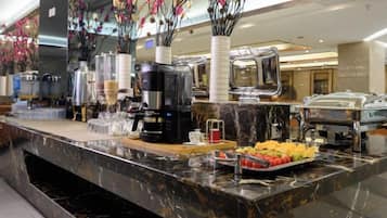 A buffet setup with various food containers, a coffee machine, and decorative flowers.