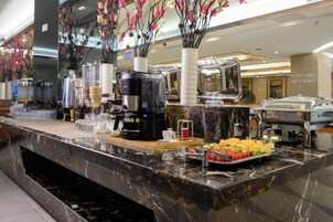 Montaje de bufé con diferentes recipientes de comida, una máquina de café y flores decorativas.
