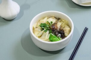 A bowl of soup with dumplings, garnished with a leaf, on a table.