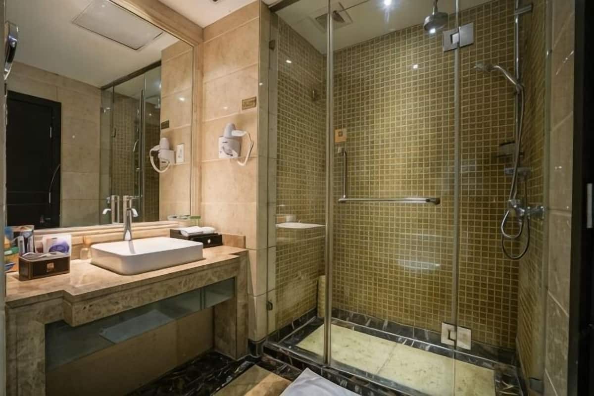 Un baño moderno con ducha envuelta en vidrio, lavabo con espejo y tocador con artículos de aseo.
