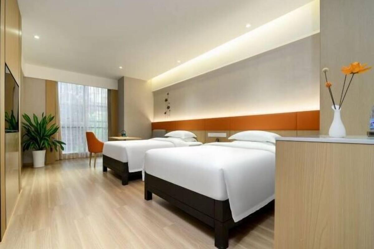 A hotel room with two beds, a desk, a chair, and a potted plant.