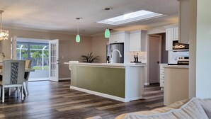 A modern kitchen with a central island, white cabinetry, and a dining area with a table and chairs.