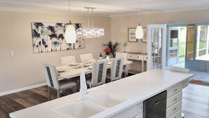 A modern kitchen with a central island, white cabinetry, and a dining area with a large painting on the wall.
