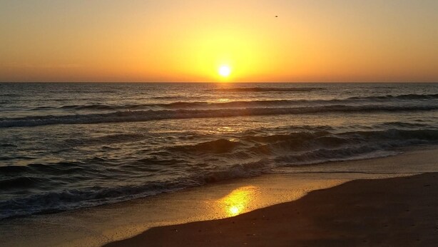 A sunset over the ocean with waves approaching the shore.