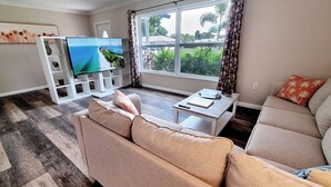 A living room with a sofa, a coffee table, a TV on a stand, and a window with curtains.