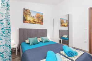 Ein modernes Schlafzimmer mit einem großen Bett, einem Nachttisch, einem Spiegel und Blick auf einen Park durch das Fenster.