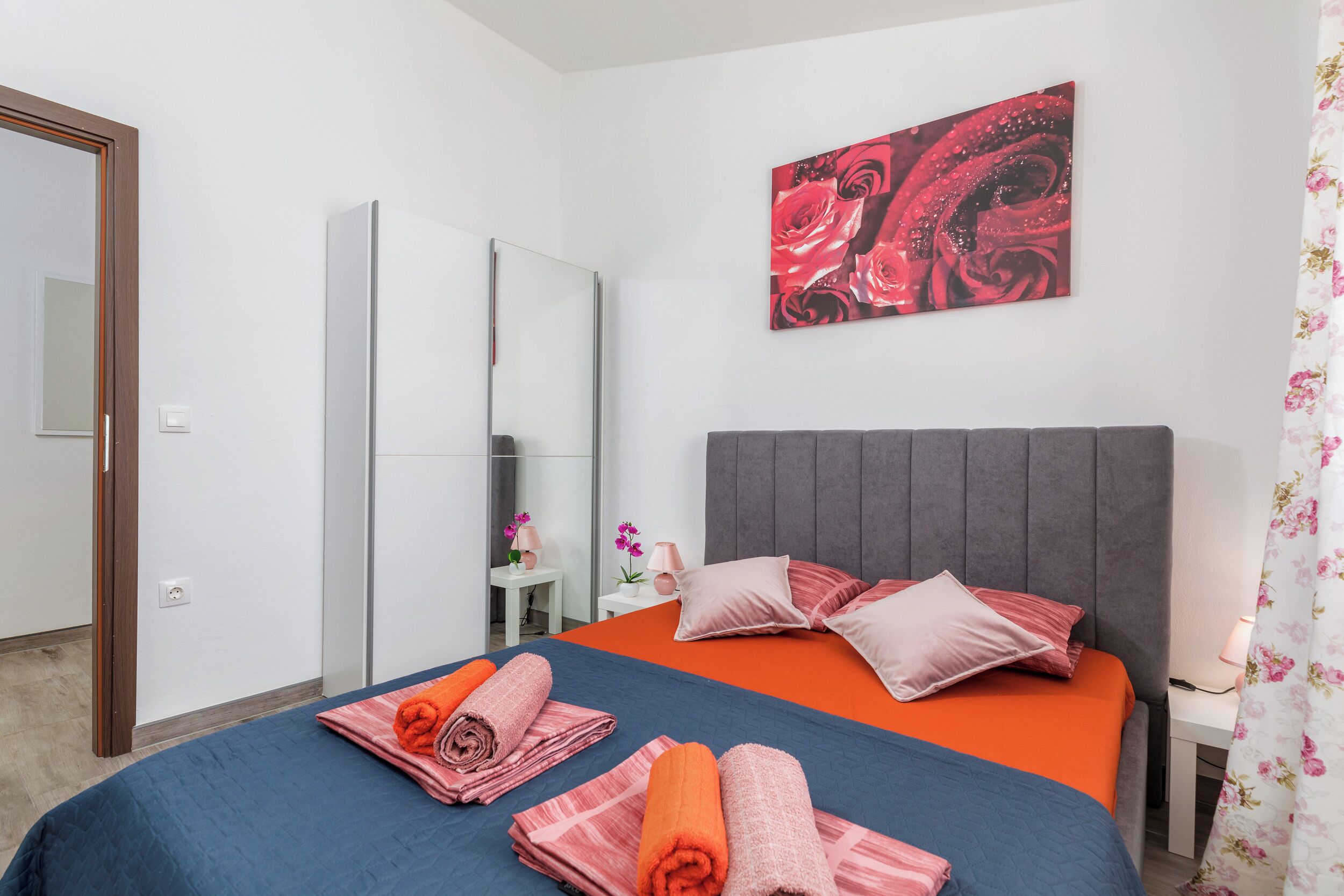 A hotel room with a bed, a wardrobe, a mirror, and a painting on the wall.