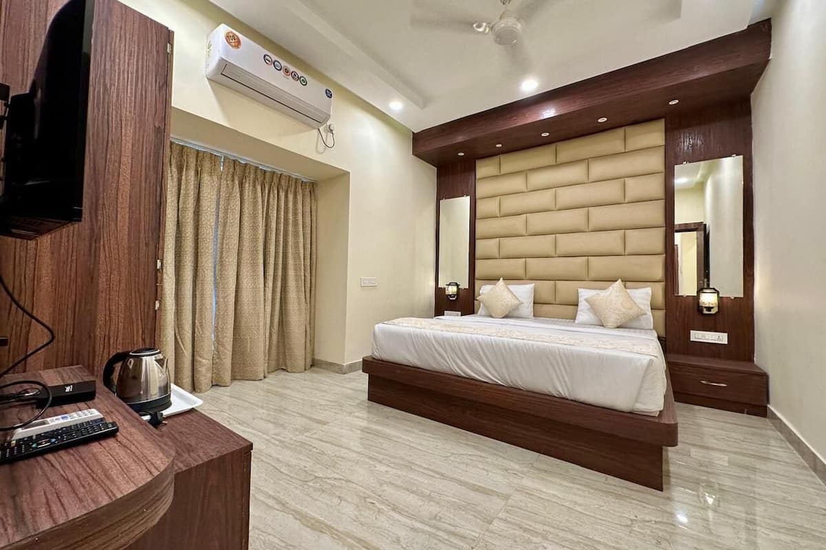 A modern hotel room with a large bed, a wooden desk, a television, and an air conditioning unit.