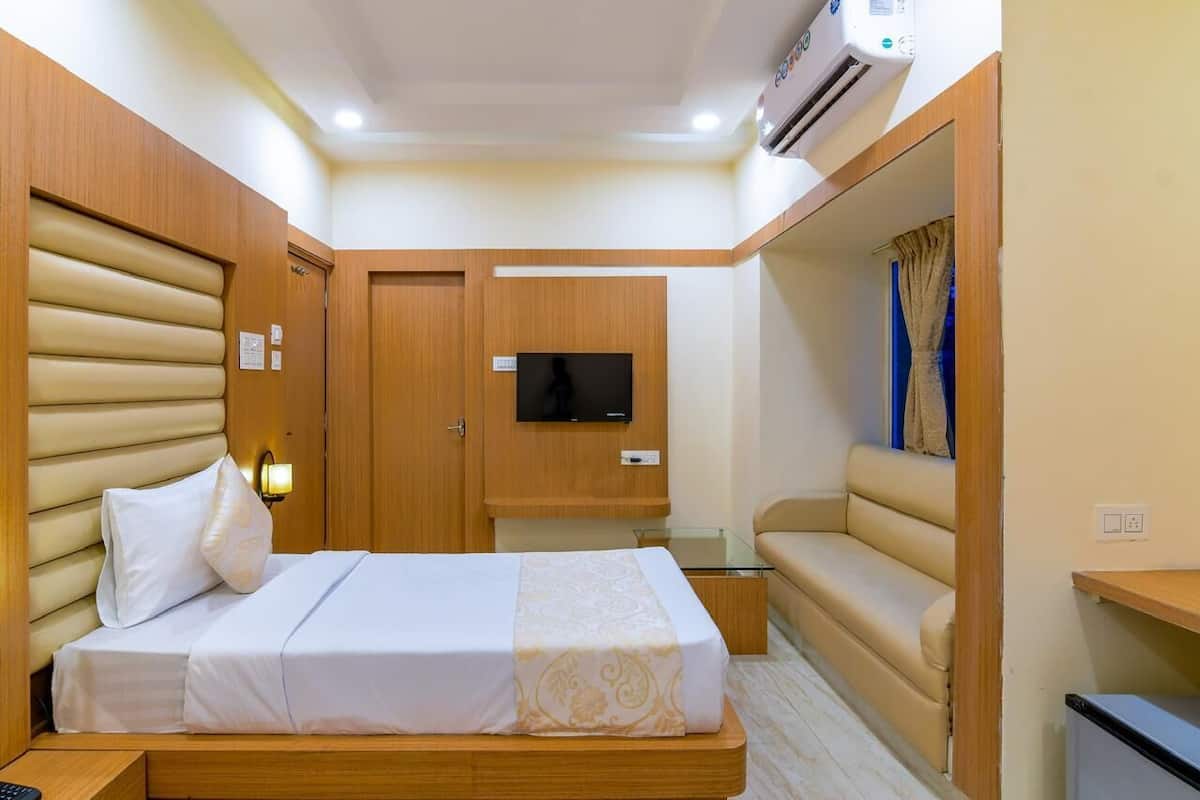 A compact hotel room with a bed, a sofa, a TV, and an air conditioning unit.