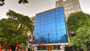 A modern building with a glass facade, likely a commercial or entertainment venue, surrounded by trees and other buildings. - The Elgin Hotel (Kolkata)