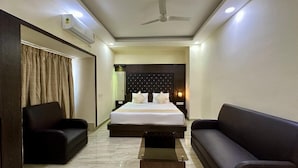 A hotel room with a bed, two sofas, a coffee table, a ceiling fan, and an air conditioning unit. - The Elgin Hotel (Kolkata)